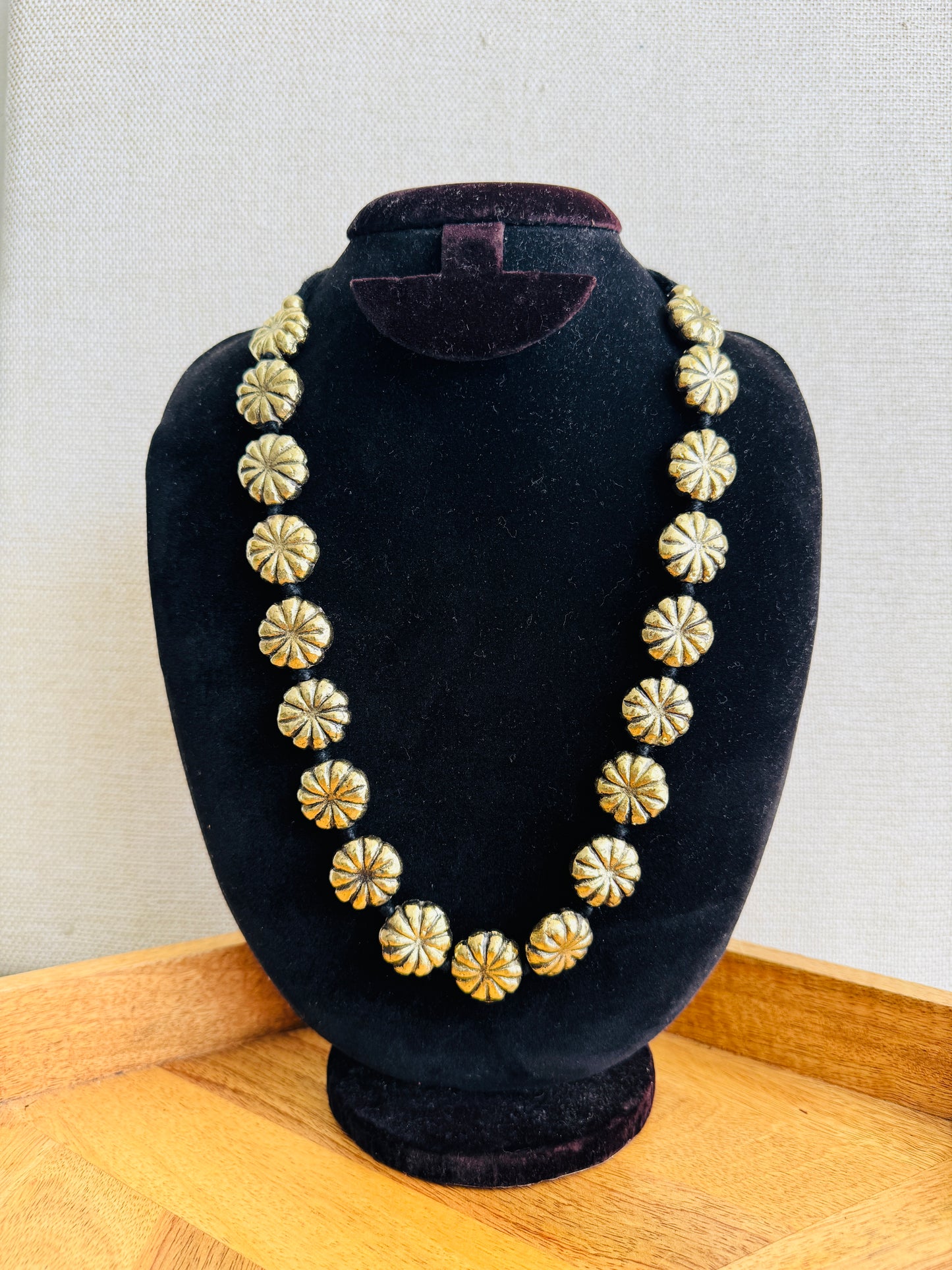 Necklace with gold and silver floral patterns on a black bust against a light background