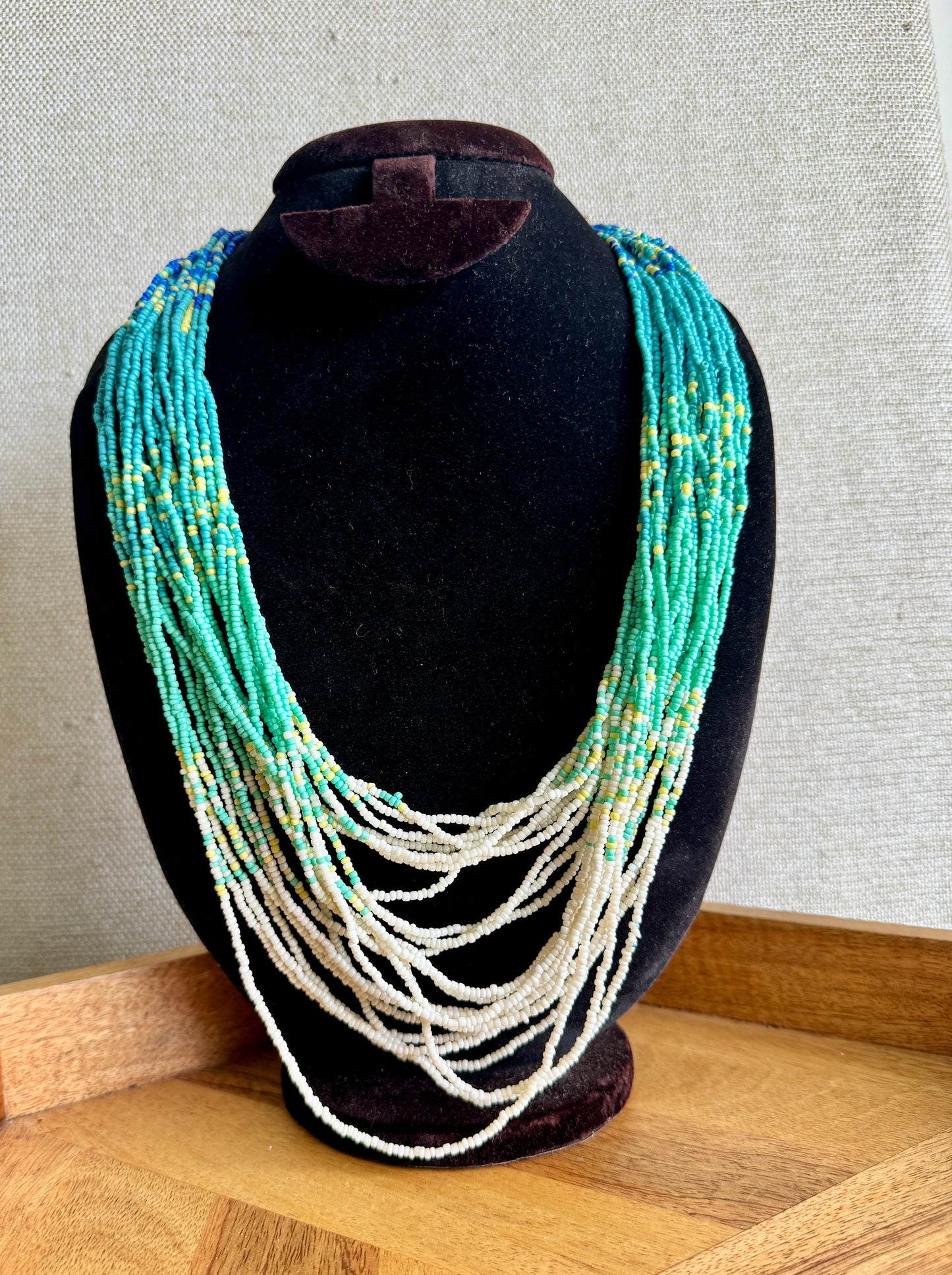 Necklace with turquoise and white beads on a black mannequin bust against a gray wall.
