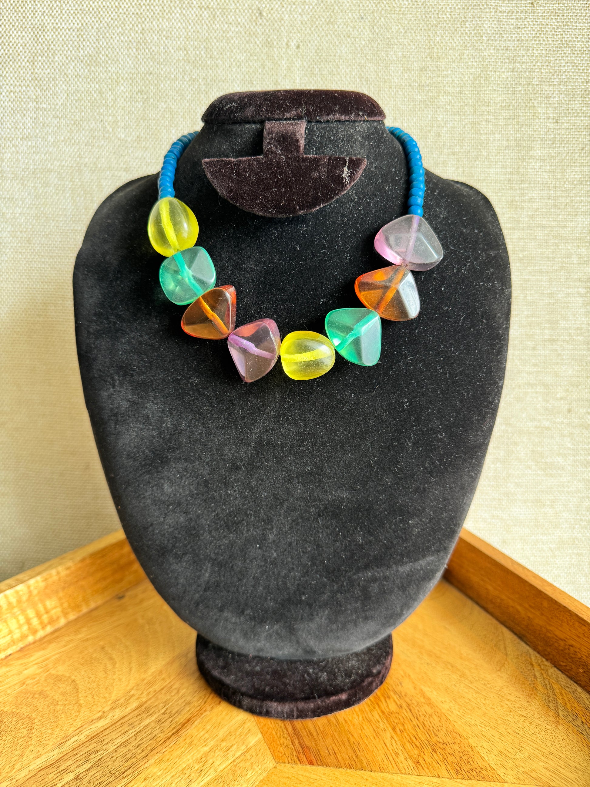 Colorful gemstone necklace on a black velvet cushion with a wooden surface in the background