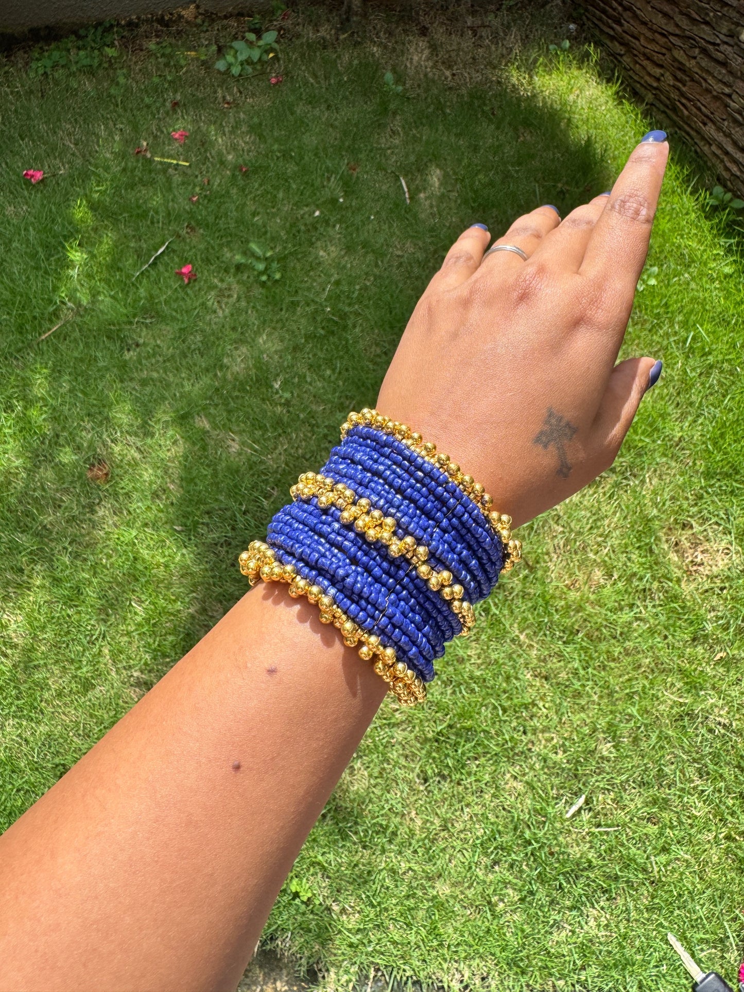 Hand wearing a blue and gold beaded bracelet on a grassy background