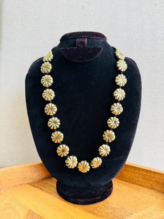 Necklace with gold and silver floral patterns on a black bust against a light background