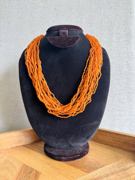 Orange necklace on a black mannequin bust against a neutral background