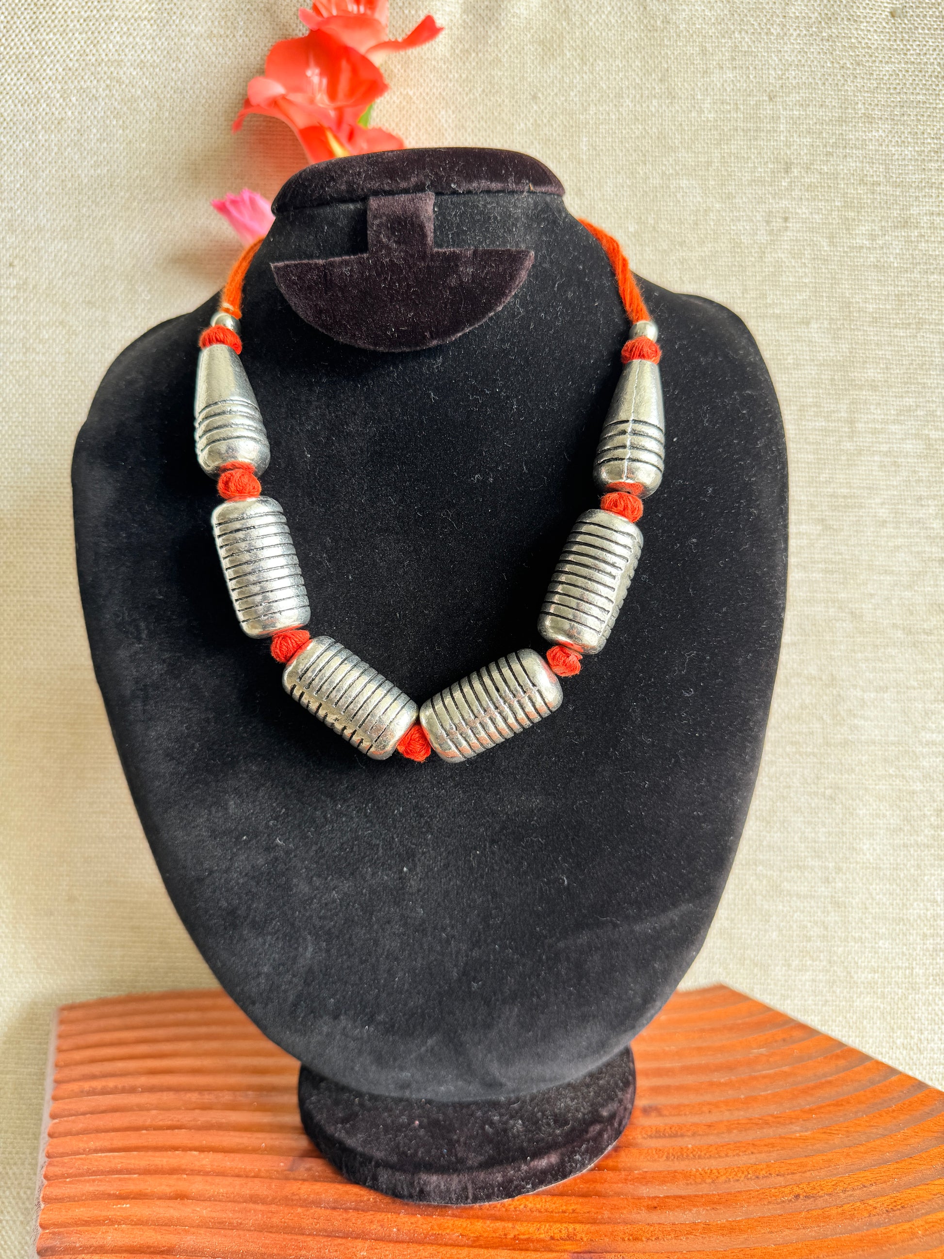 Silver beaded bracelet with red accents on a orange thread velvet stand.