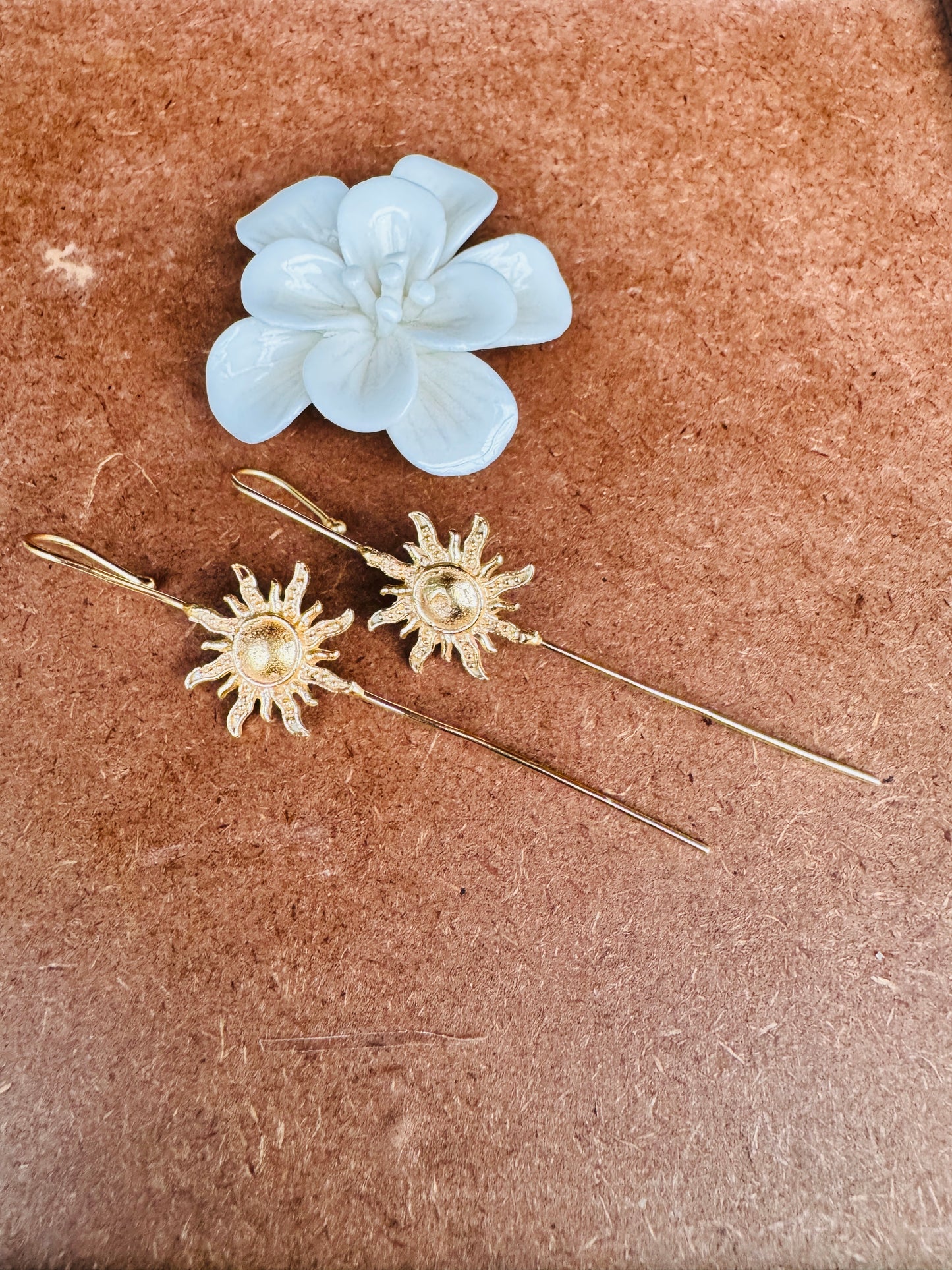 Gold sun-shaped earrings with pearl-like centers on a brown surface.