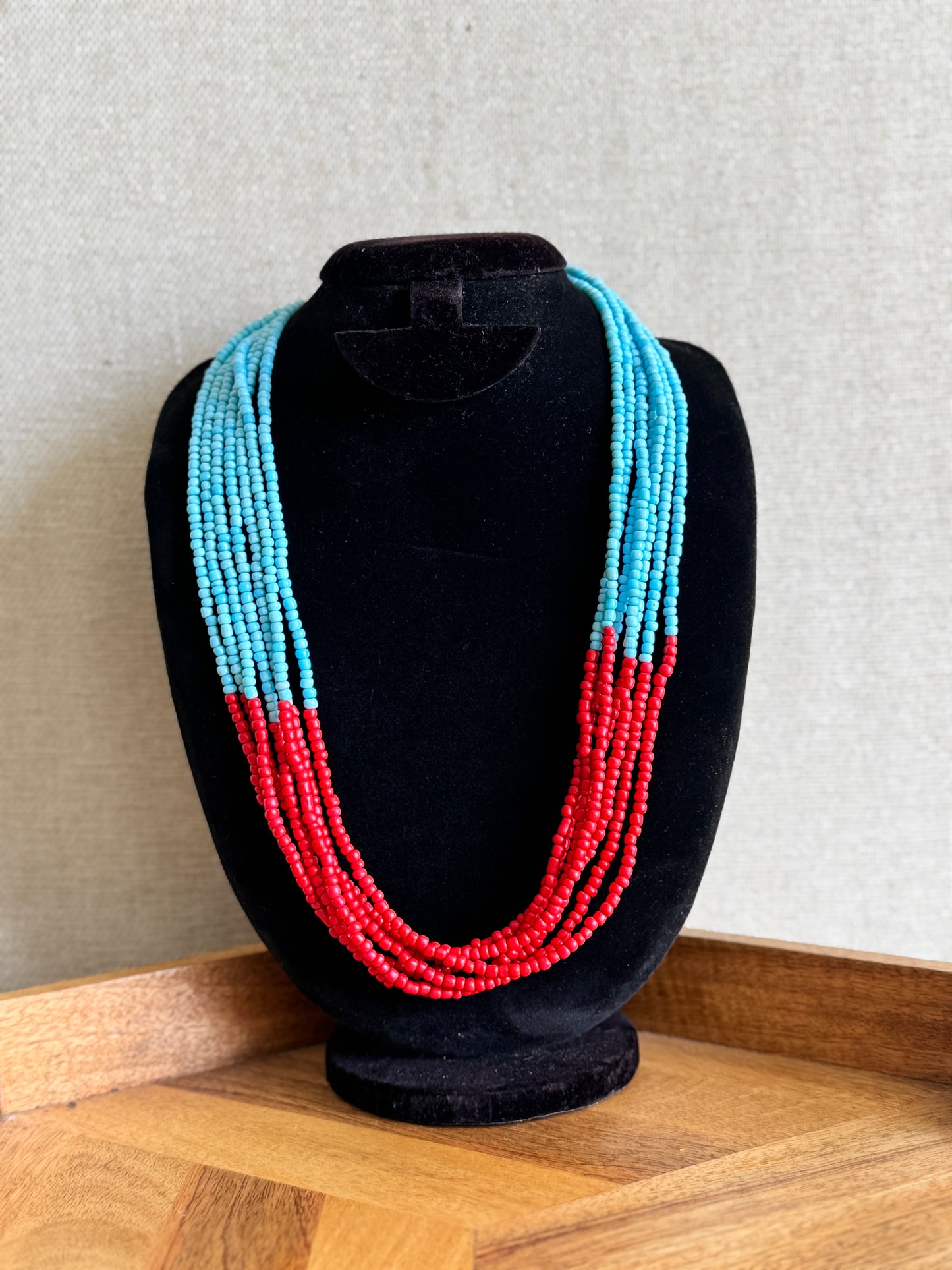 Necklace with blue and red beads on a black mannequin bust against a neutral background
