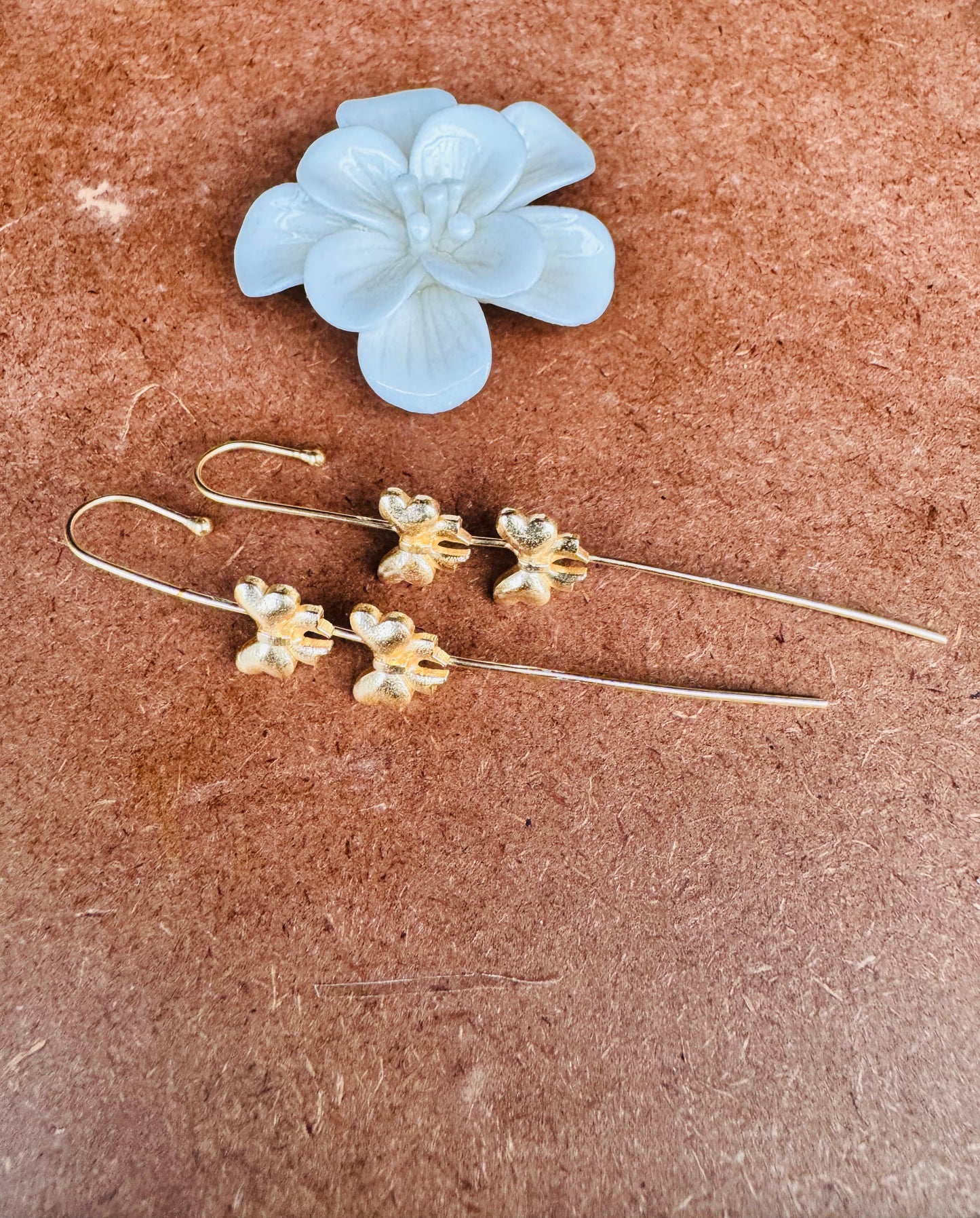 Gold floral earrings on a brown surface with a white flower above them