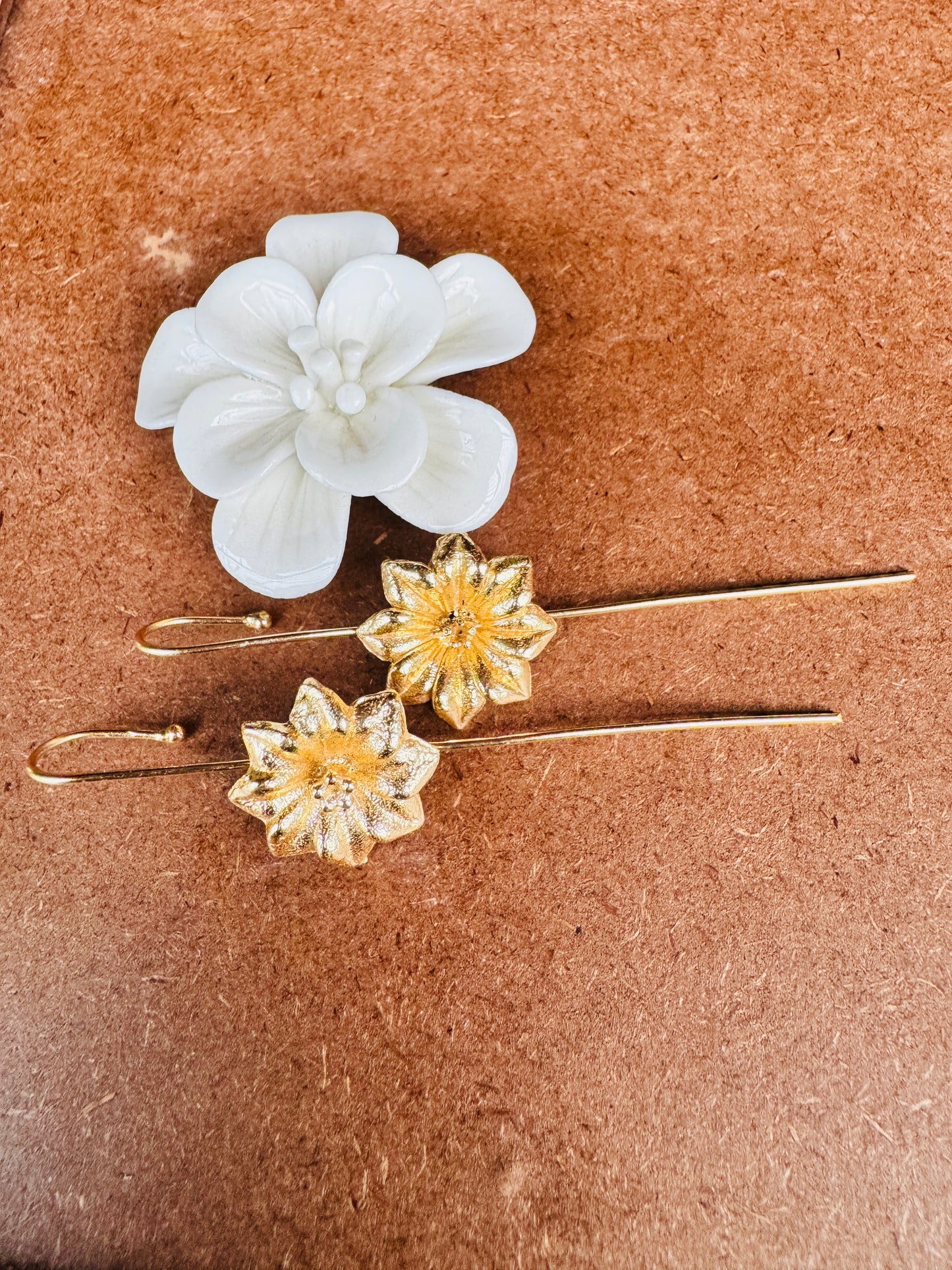 Floral ear pins with gold and white flowers on a brown surface