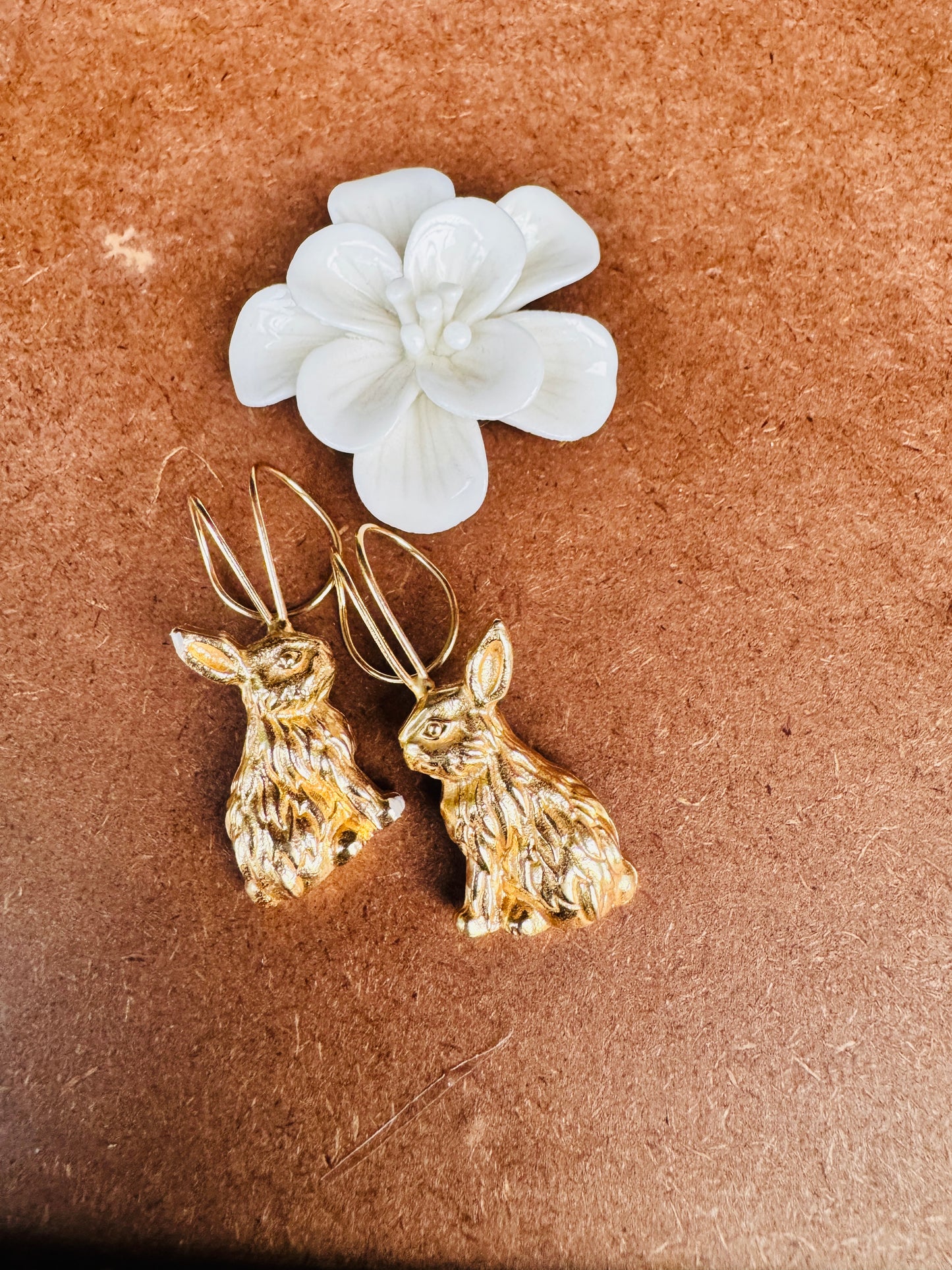 Gold rabbit-shaped earrings on a brown surface with a white flower.