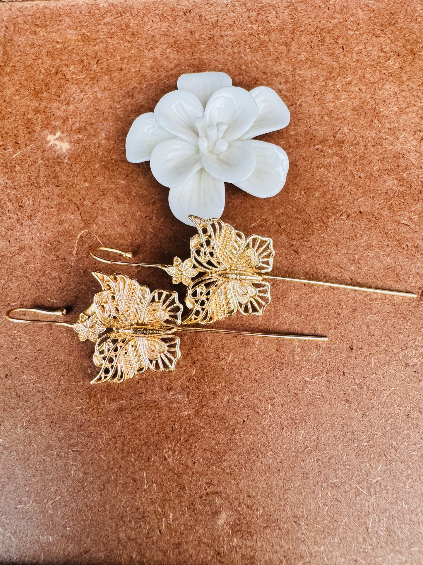 Brass ear pins with butterfly designs and a white flower on a brown surface