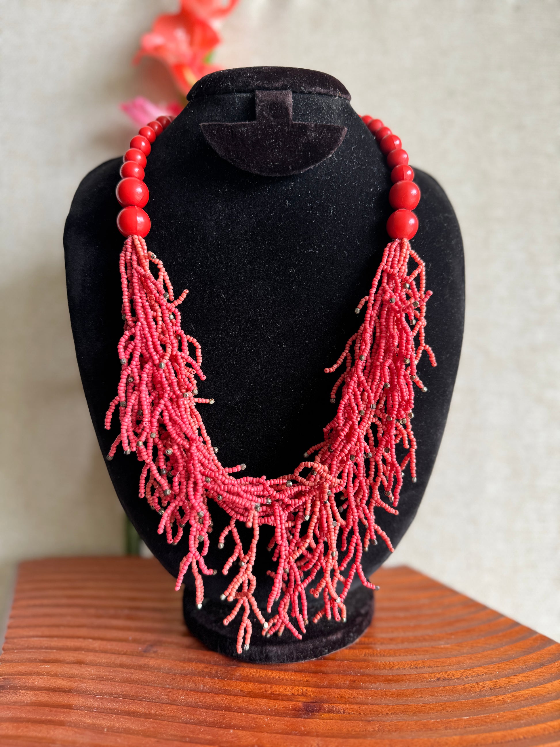 Necklace with red beads on a black stand against a neutral background
