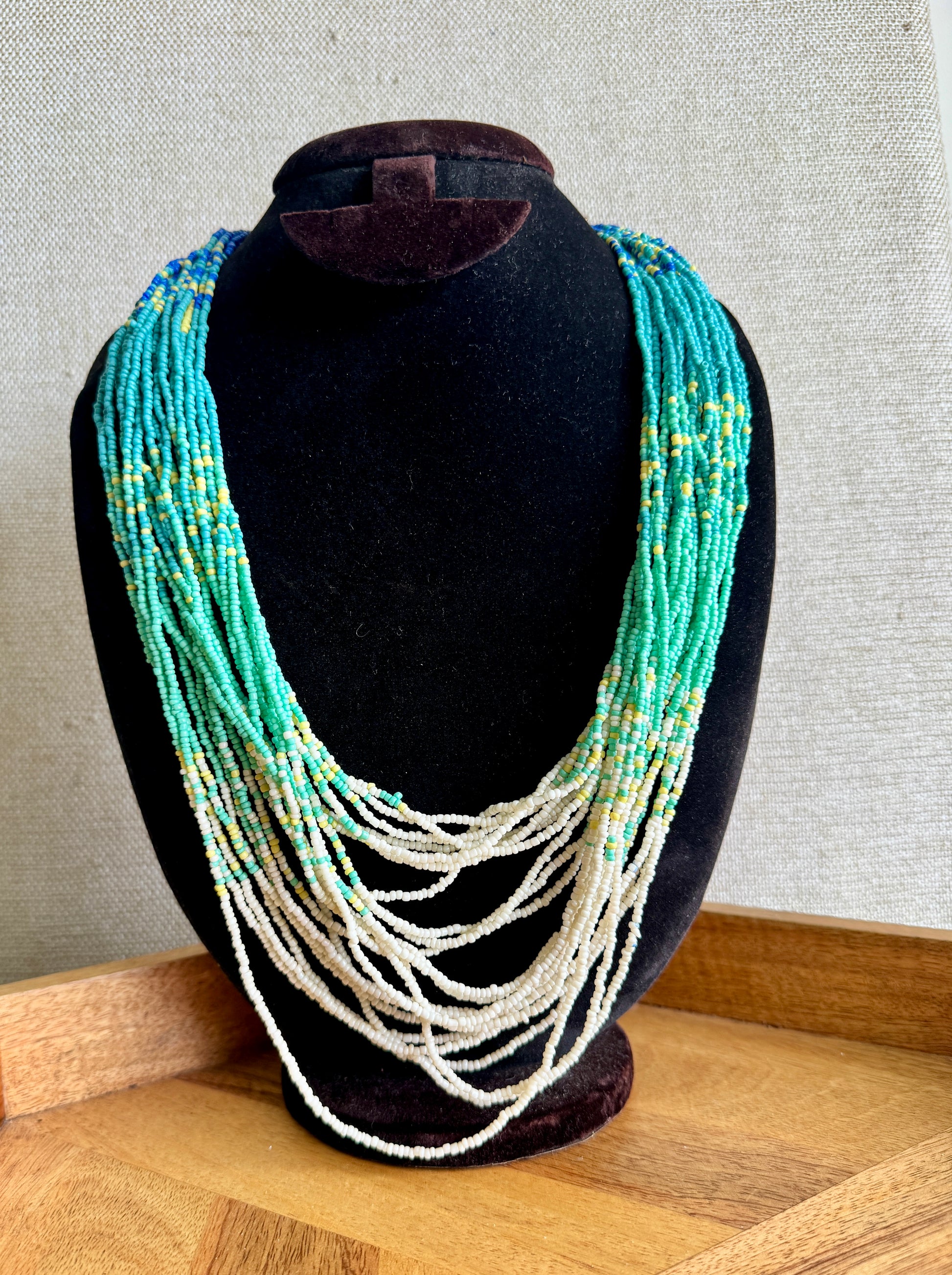 Necklace with turquoise and white beads on a black mannequin bust against a gray wall.