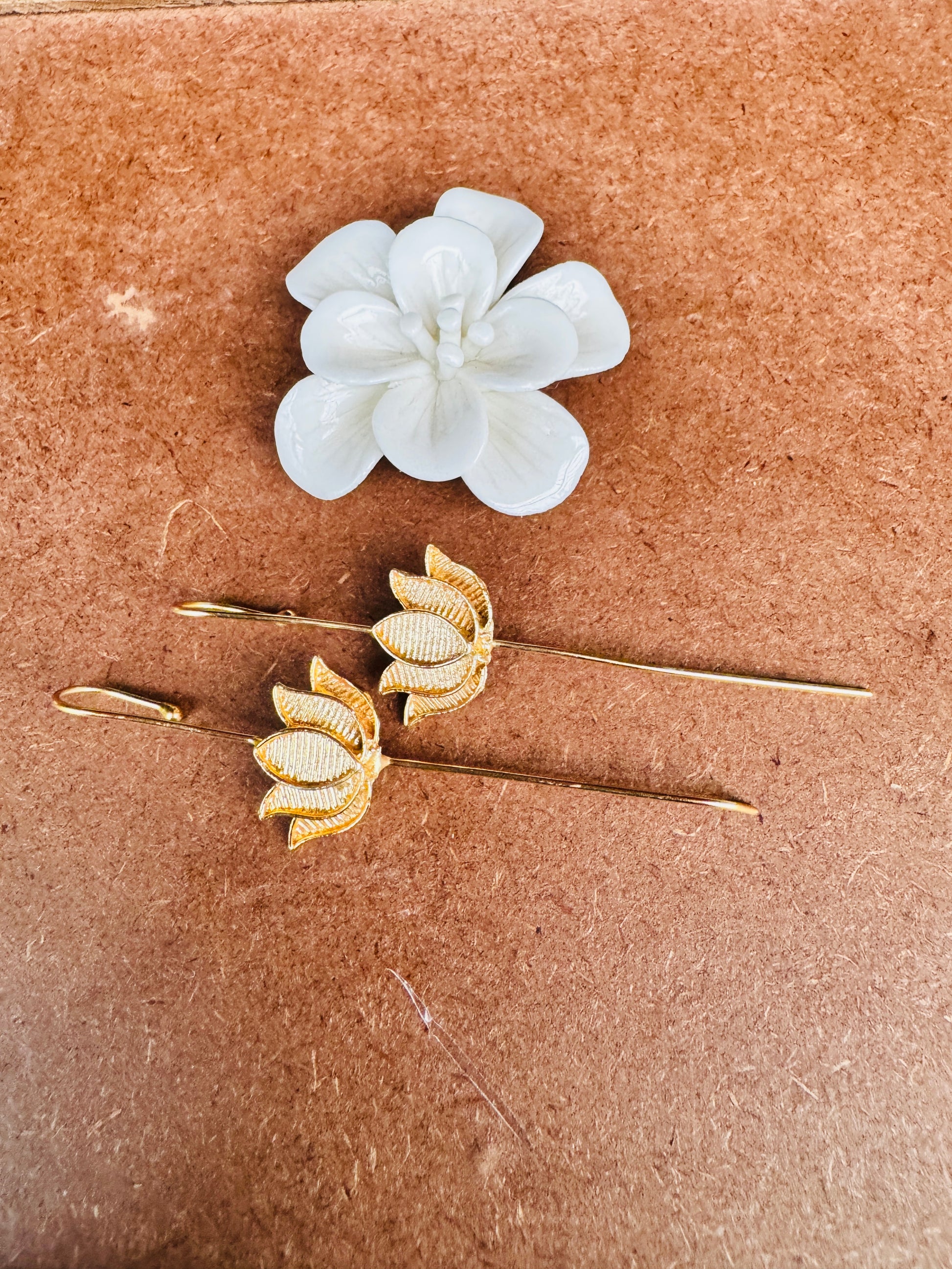 Lotus Gold floral earrings on a brown surface with a white flower above them.