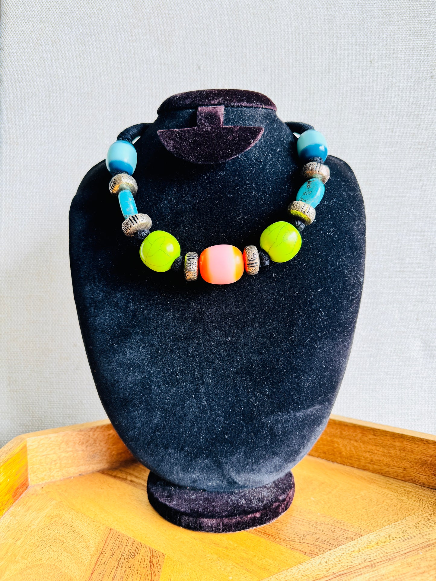 Necklace with colorful beads on a black velvet stand against a light gray background