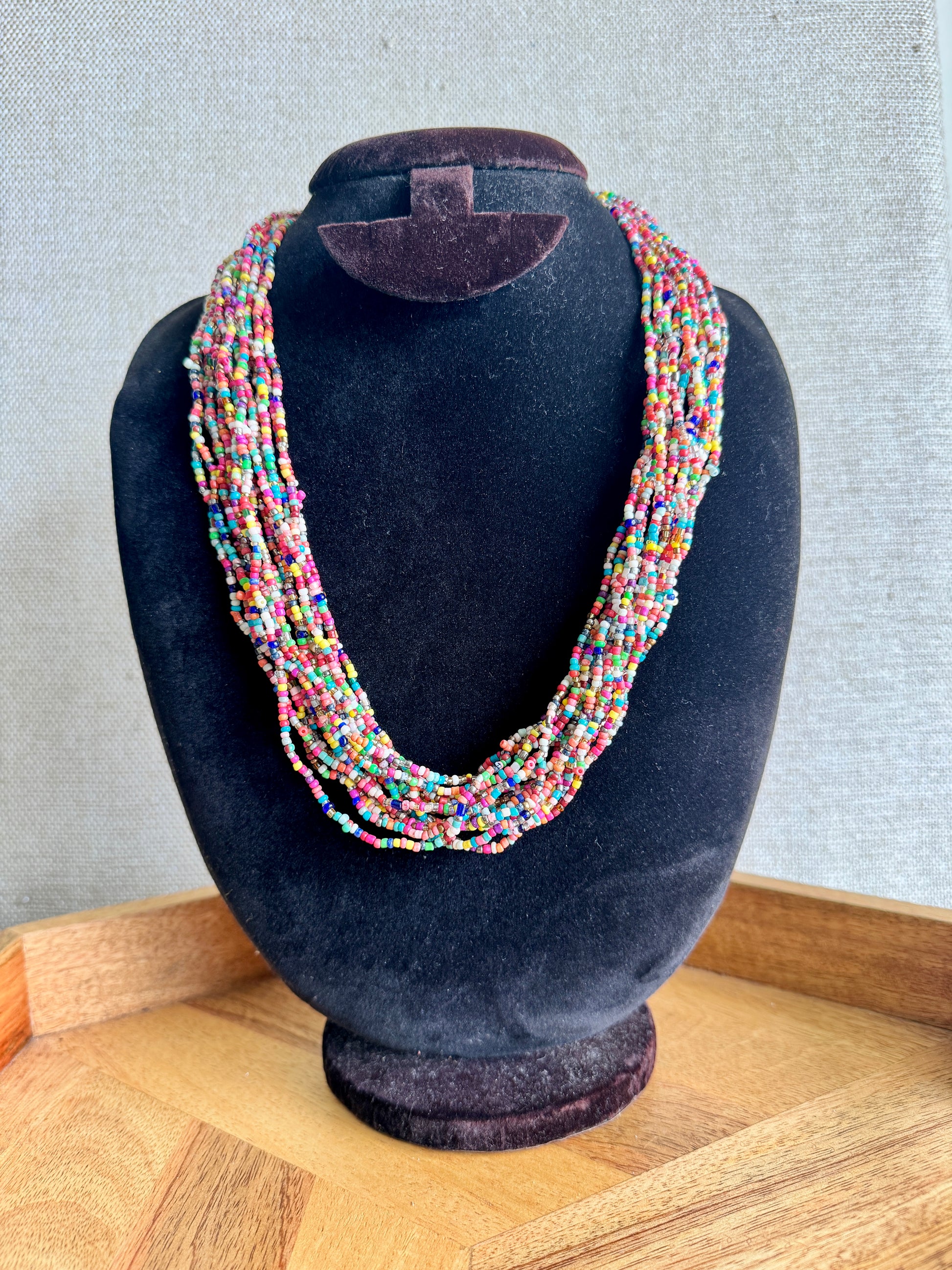 Multicolored beaded necklace on a black velvet mannequin bust against a neutral background.