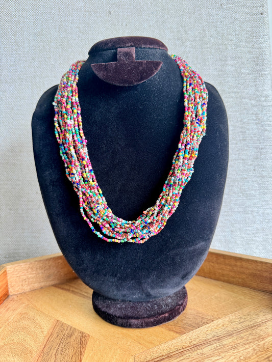Multicolored beaded necklace on a black velvet mannequin bust against a neutral background.