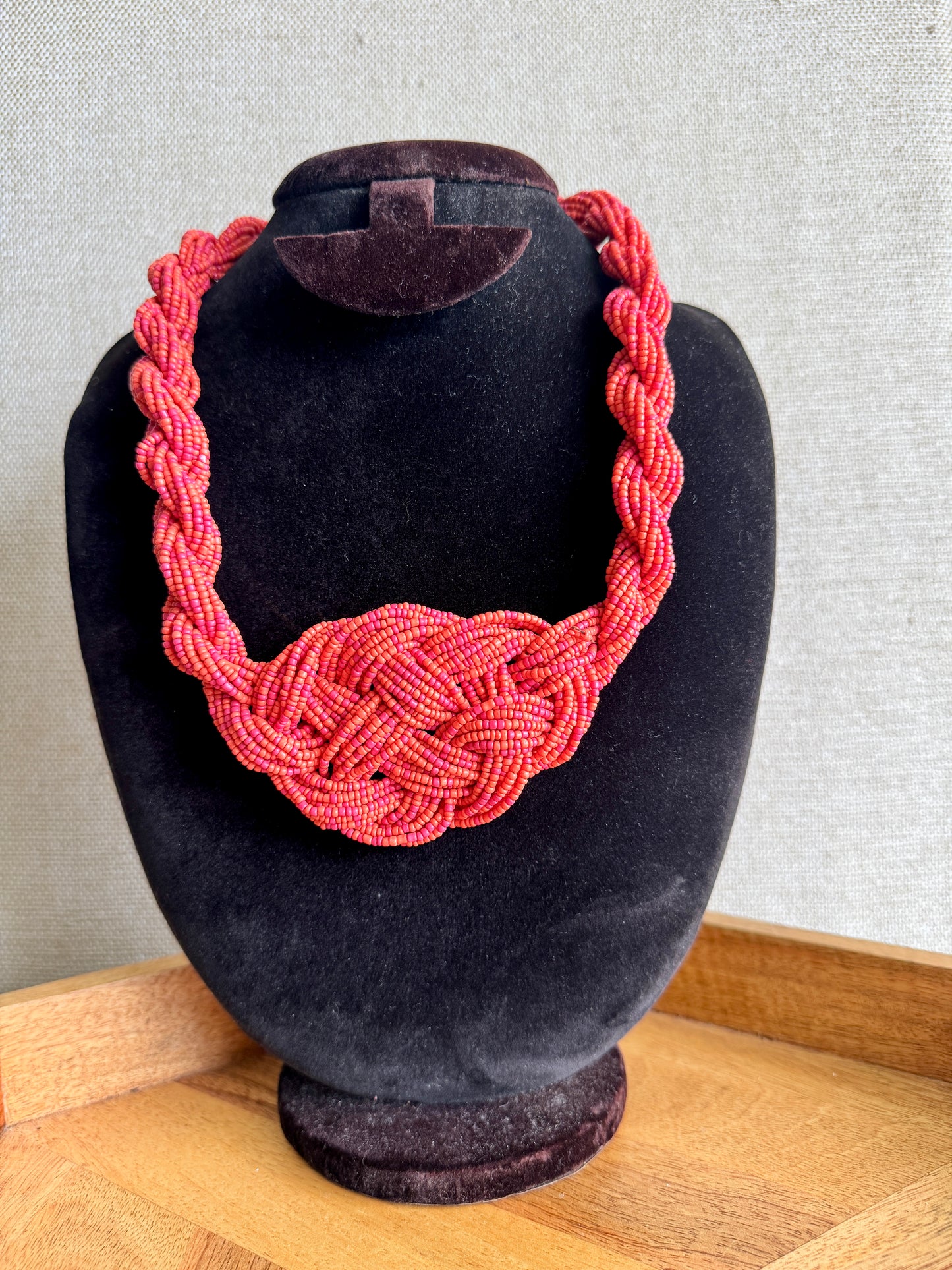 Red braided necklace on a black velvet mannequin bust against a neutral background
