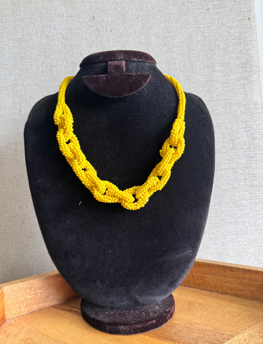Yellow beaded necklace on a black mannequin bust against a gray wall.